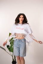 Woman wearing a white tassel top and denim shorts on a plain background