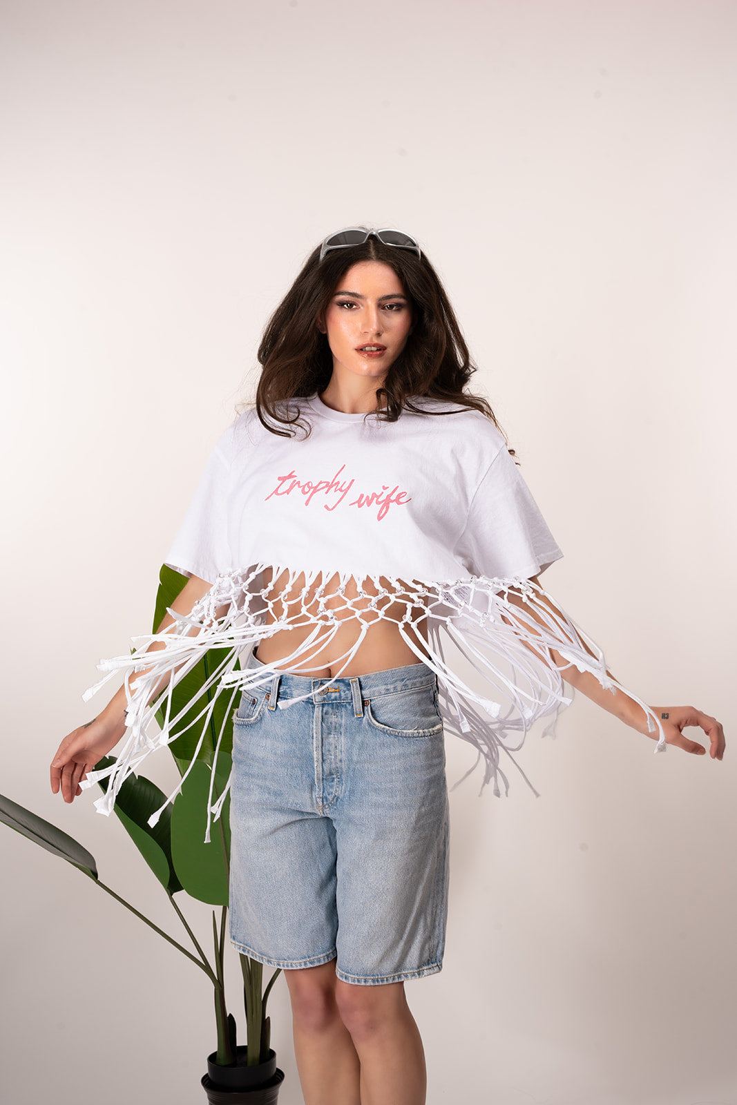 Woman wearing a white tassel top and denim shorts on a plain background