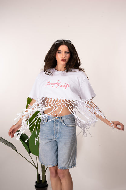 Woman wearing a white tassel top and denim shorts on a plain background