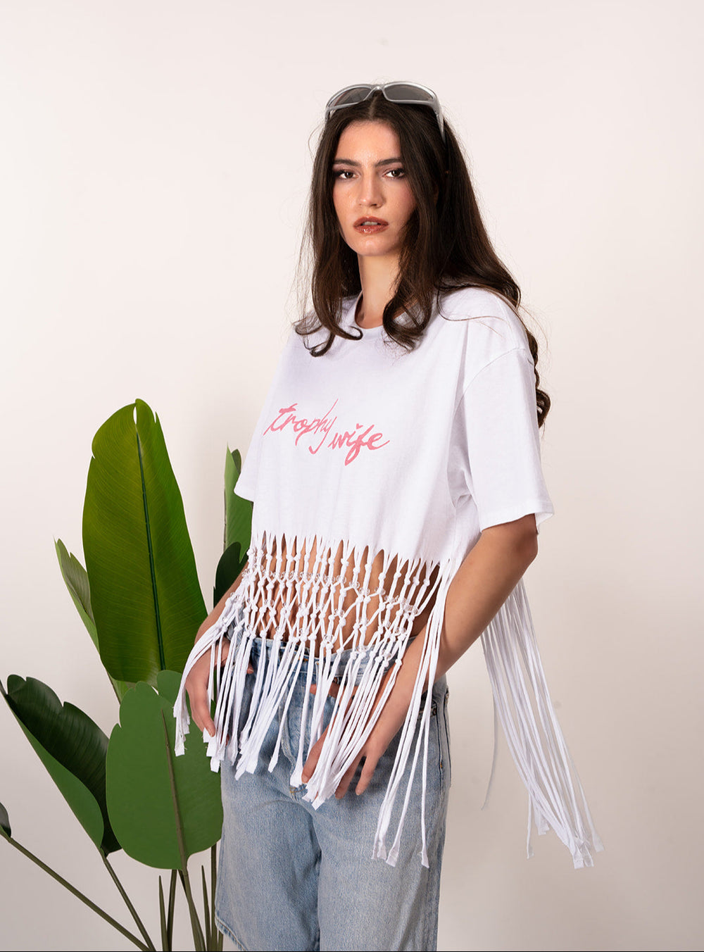 Woman wearing a white fringe top over a white t-shirt with text, standing against a plain background.