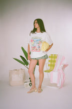Woman wearing a graphic t-shirt and shorts with a plant and chair in the background