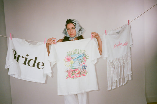 Woman holding a t-shirt with 'Bride' and another with floral design, standing between two similar shirts on a line.